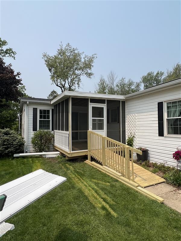 Screened porch addition with wooden accessibility ramp on a white-sided home