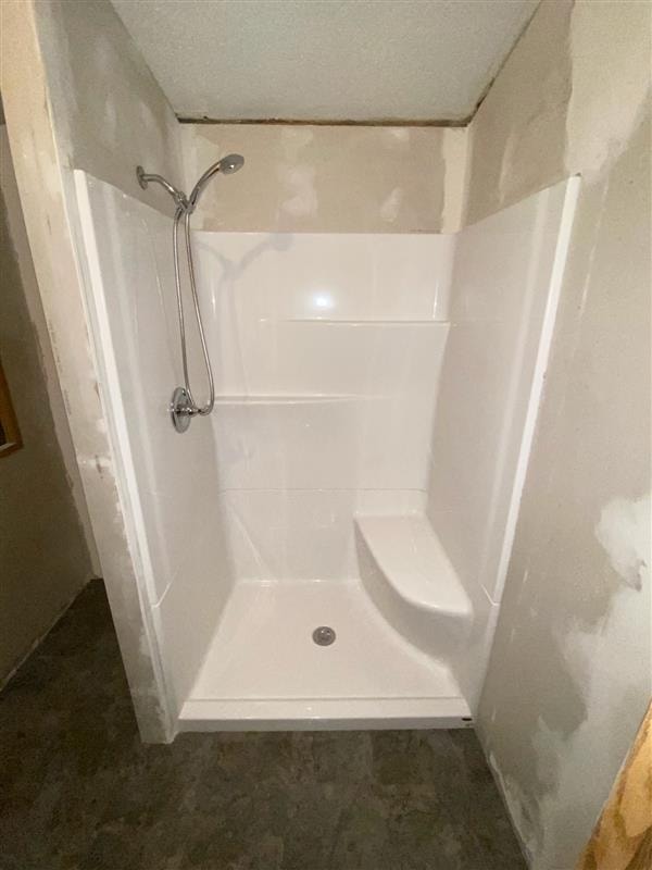 Newly installed white shower enclosure with built-in seat and handheld fixture